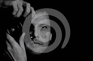 Black and white portrait of a photographer with an open eye with an old SLR camera on a dark background close-up