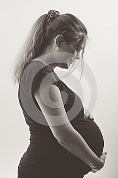 Black and white portrait of pregnant woman in profile with hands on her stomach on white background, future life concept