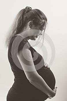 Black and white portrait of pregnant woman in profile with hands on her stomach on white background, future life concept