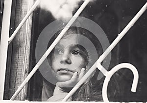 Black and white portrait of Sad little girl looks through window