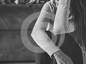 Black and white portrait of sad young woman sitting by sofa