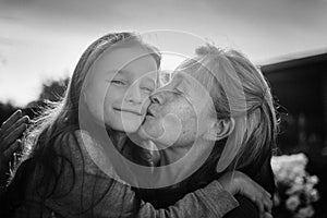 Black and white portrait of senior grandmother with gray hair with her little granddaughter hugging in the garden and