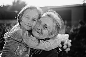 Black and white portrait of senior grandmother with gray hair with her little granddaughter hugging in the garden and