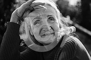 Black and white portrait of senior woman with grey hair and face with wrinkles outdoors relaxing at the park