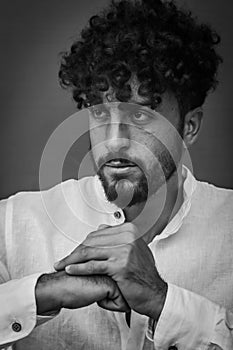 Black and white portrait of a serious young man with beard and curly hair, holding his fist with his other hand and looking menaci