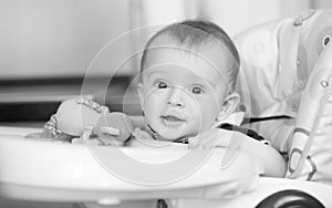 Black and white portrait of smiling baby boy sitting in highchair at kitchen