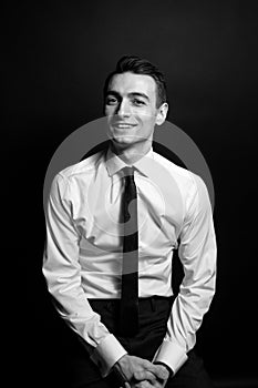 Black and white portrait of a smiling young man in a white shirt and black tie, looking at the camera