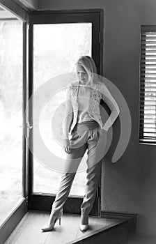 Black and white portrait of sophisticated blonde woman posing next to a window with natural light