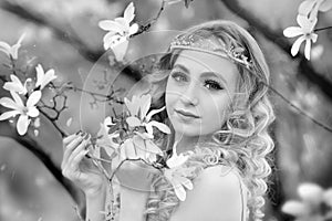 Black-white portrait of stunning young beauty blonde with jewelry for hair in the garden where magnolia trees bloom.  Jewelry for