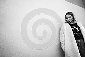 Black and white portrait of a stylish woman posing against a grey background while lying against the wall