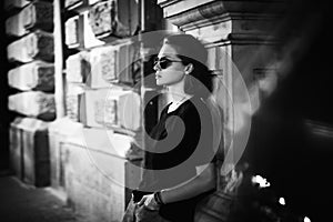 Black and white portrait of stylish young woman in sunglasses sitting in profile