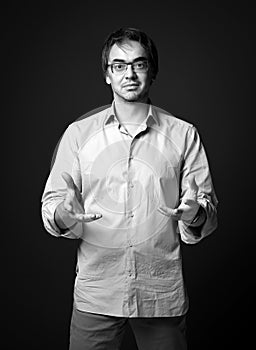 Black and white portrait of unshaved adult man in shirt and jeans standing holding out hands to us, palms up