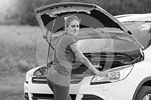 Black and white portrait of woman standing at broken car with op