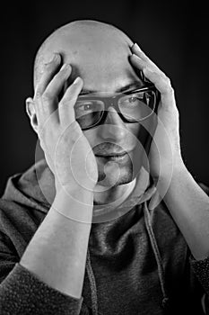 Black and white portrait of a young bald man with black eyeglasses holding his head in his hands