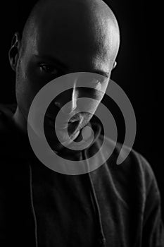 Black and white portrait of a young bald man in the dark with a serious and scary look