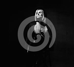 Black and white portrait of young beautiful positive blond woman in stylish casual clothing and hat sitting over dark background