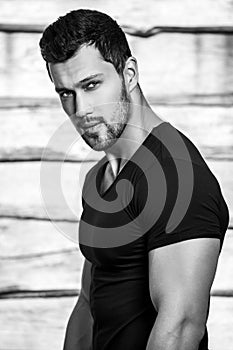 Black-white portrait of young beautiful sporty man in black t-shirt against wooden wall