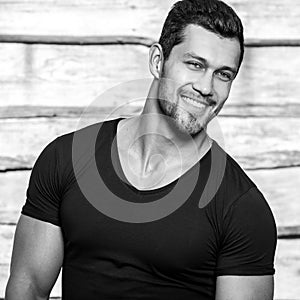 Black-white portrait of young beautiful sporty man in black t-shirt against wooden wall