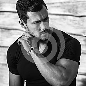 Black-white portrait of young beautiful sporty man in black t-shirt against wooden wall