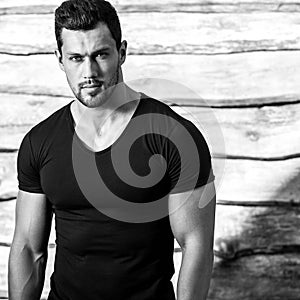 Black-white portrait of young beautiful sporty man in black t-shirt against wooden wall