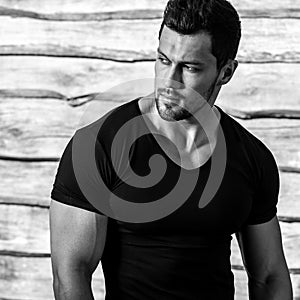 Black-white portrait of young beautiful sporty man in black t-shirt against wooden wall