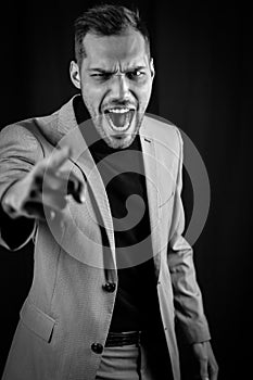 Black and white portrait of a young businessman in a gray suit, very angry yelling and gesturing accusingly in front of him