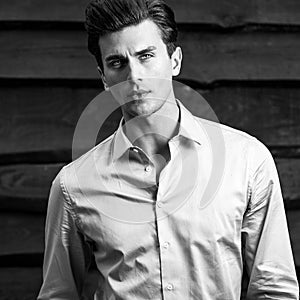 Black-white portrait of young handsome fashionable man against wooden wall