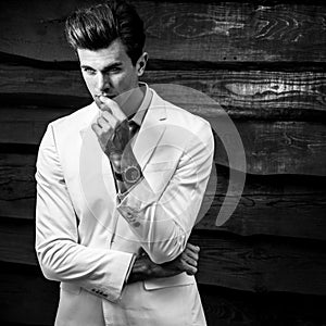 Black-white portrait of young handsome fashionable man in white suit against wooden wall