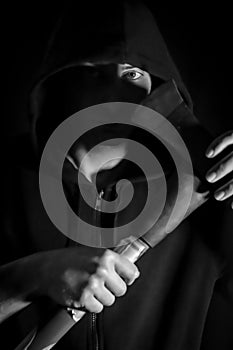 Black and white portrait of a young hooded man with blue eyes who with an ax in his hand has a disturbing look