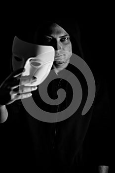 Black and white portrait of a young hooded man taking off his mask, concept for being true and authentic