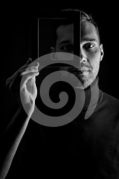 Black and white portrait of a young man holding a frame in front of his face, concept for the uniqueness of individuals