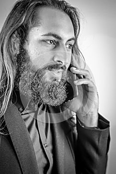 Black and white portrait of a young middle eastern businessman with beard and long hair while having a conversation on the mobile