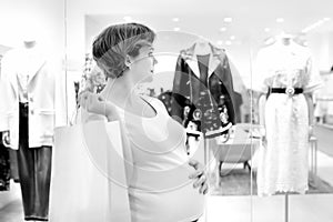 Black and white portrait of young pregnant woman is watching the showcase of baby store in shopping mall
