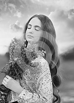 Black and white portrait with a  young redhead girl holding a bouquet of lilac lupins in her hands, closing her eyes. Enjoying