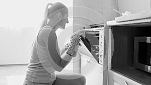 Black and white portrait of young smiling woman baking tasty sweet cookies in the oven at home on kitchen