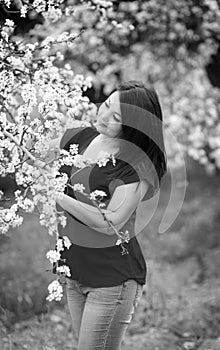 Black and white portrait of a young woman holding a brunch of blossoming plum tree in garden, happily smiling