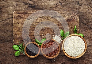 Black, white and red quinoa in spoons, raw quinoa groats assorted, wooden rustic kitchen table, top view