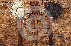 Black, white and red quinoa in spoons, raw quinoa groats assorted, wooden rustic kitchen table, top view