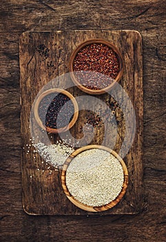 Black, white and red quinoa in spoons, raw quinoa groats assorted, wooden rustic kitchen table, top view