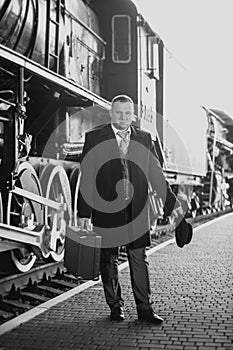 Black and white retro photo of man in suit waiting for train