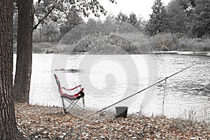 Black and white retro style photo of red fishing chair near fishing rod and fishing bait on river bank in summer