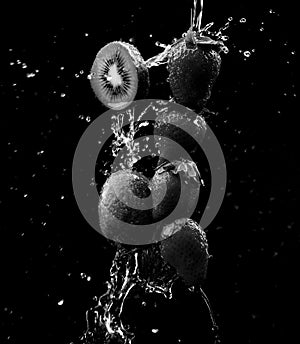 a black and white of a Row of strawberries and kiwi being doused with plenty of water against a black background