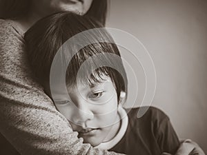 Black and white sad boy being hugged by his mother at home.