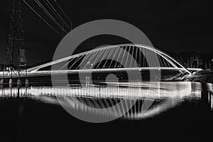 Black and white scene of an illuminated walking bridge at Sompasaari, Helsinki during night time.