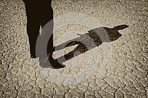 Black and White  Sepia Image of a Manâ€™s legs casting full body shadow on dry lake bed