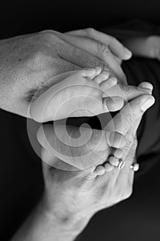 Black and white shade beautiful shape hands of mother, hold tiny newborn baby feet on black background with love,
