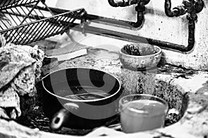 Black-and-white shot of dirty bowls put on the stony sink and some pipes