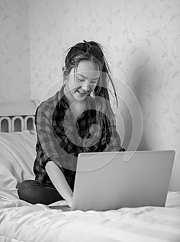 Black and white shot of teenage girl sitting on bed and using la