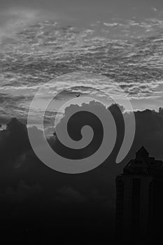 A black and white silhouette of a high rise skyscraper with a dramatic cloud and a sunset sky in the