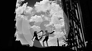 Black and white silhouettes of two people in love dancing against the beautiful sky.